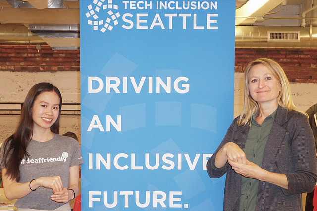 aimee and echo stand in front of tech inclusion banner partially signing "Incusive"